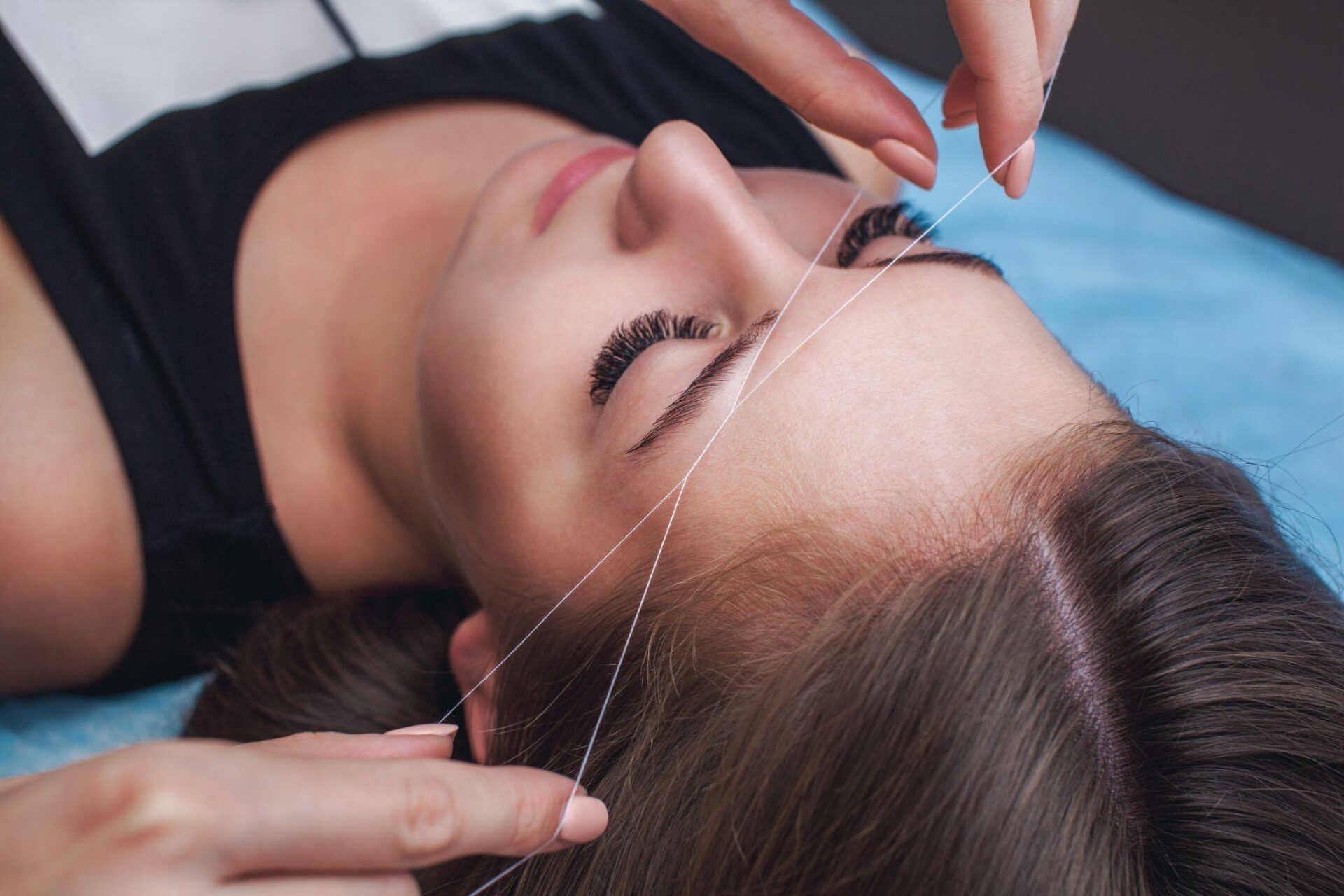 A young woman undergoes an eyebrow threading session.